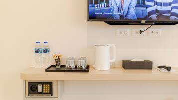 Habitación de hotel con una televisión montada que muestra una serie de Netflix, un minibar con botellas de agua, vasos, una cafetera, una caja de pañuelos y un control remoto.