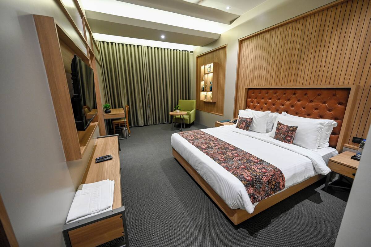 A hotel room with a large bed, a desk, a chair, a small table, and a mirror.