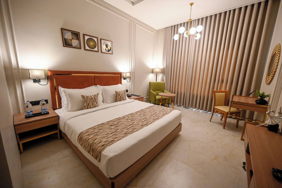 A hotel room with a large bed, bedside tables, a desk, a chair, and a lamp.