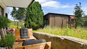 A wooden deck with two chairs and a table, surrounded by a stone wall and a variety of flowers. - Apartment 'Bäuerle' with Private Terrace, Private Garden and Wi-Fi (Schönwald)