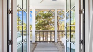 A covered outdoor area with a wooden deck, glass doors, and a view of trees and a fence. - 30A Luxury-5 Bed/Sleeps 12-Bikes-Golf Cart-Pools-Tennis/Pickleball Beach Service (Santa Rosa Beach)
