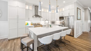 A modern kitchen with white cabinetry, a central island with bar stools, stainless steel appliances, and pendant lighting. - 30A Luxury-5 Bed/Sleeps 12-Bikes-Golf Cart-Pools-Tennis/Pickleball Beach Service (Santa Rosa Beach)
