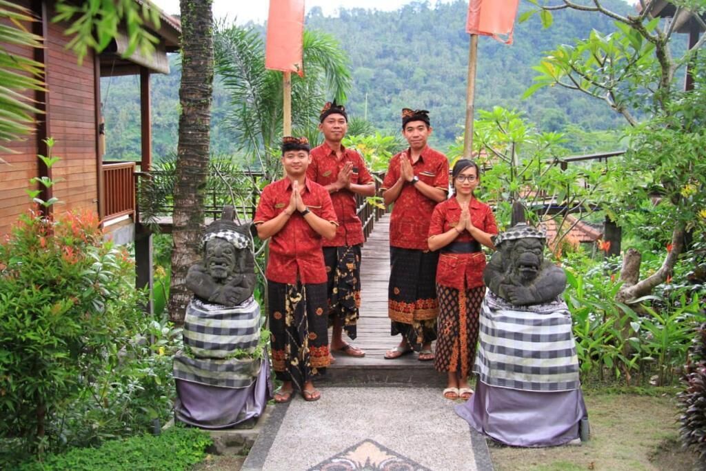 A group of people in traditional attire standing in a garden with stone statues and a wooden building in the background.