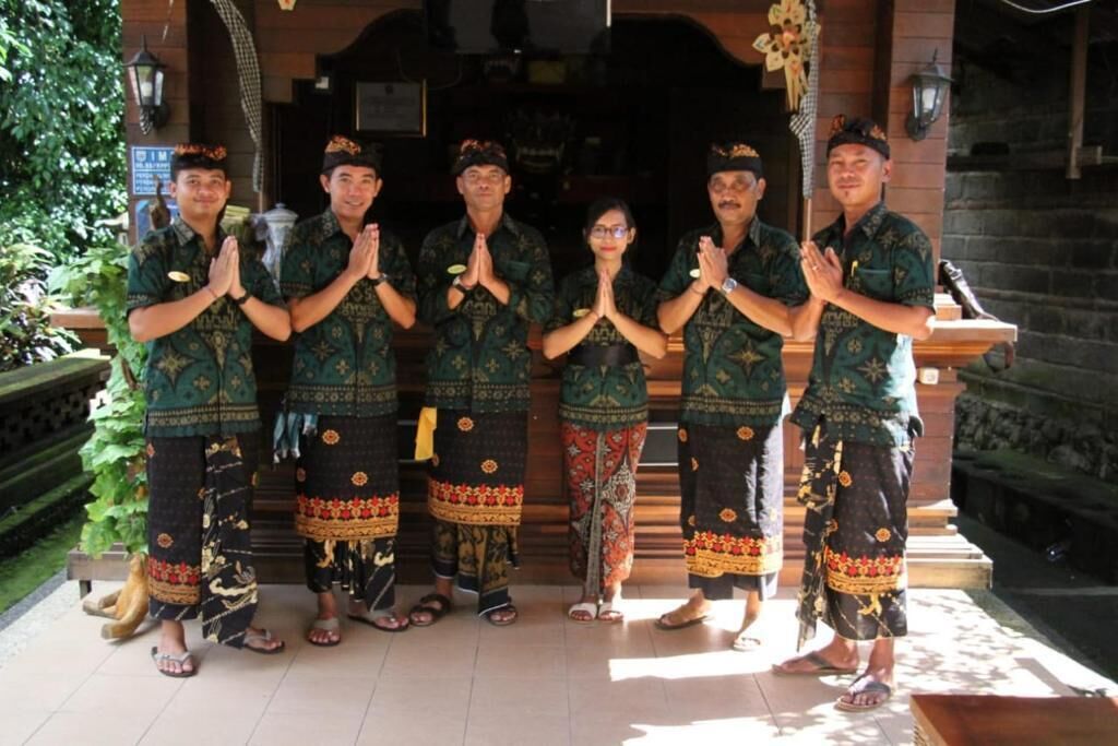 A group of people in traditional attire standing in front of a building with a tiled floor and a stone wall.