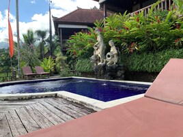 Un área de piscina con terraza de madera, sillas de descanso y una estatua de figuras.