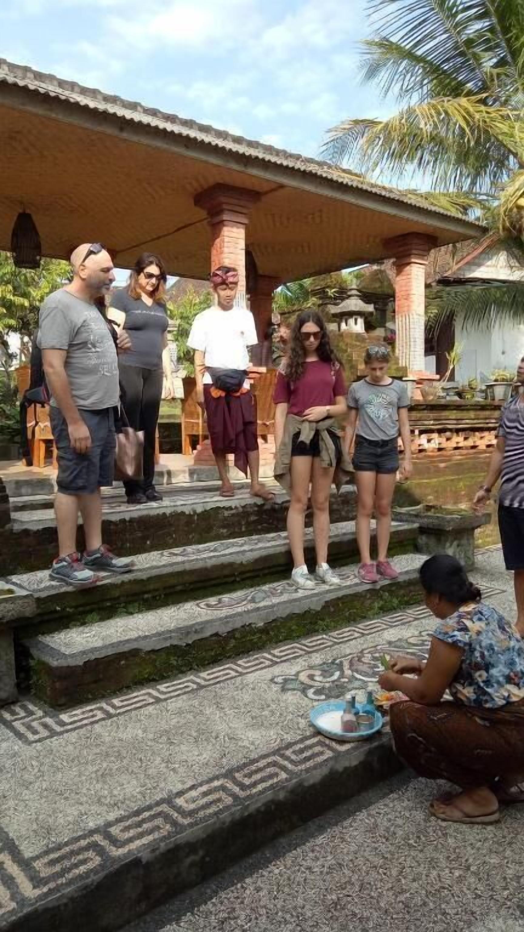 A group of people standing on stone steps with a patterned floor, under a covered area with columns.