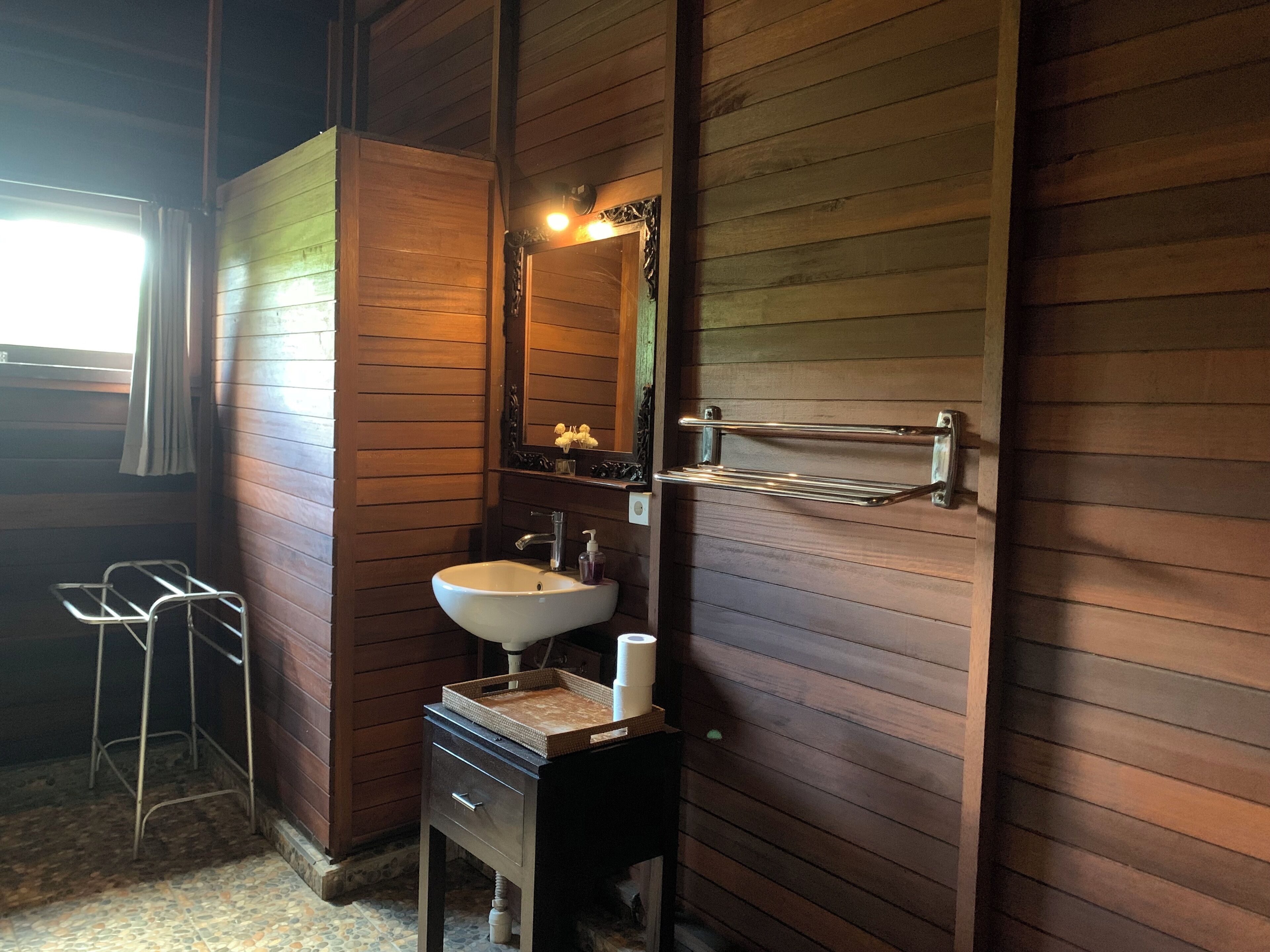 Ein Badezimmer aus Holz mit Waschbecken, Spiegel, Handtuchhalter und einer kleinen Bank.