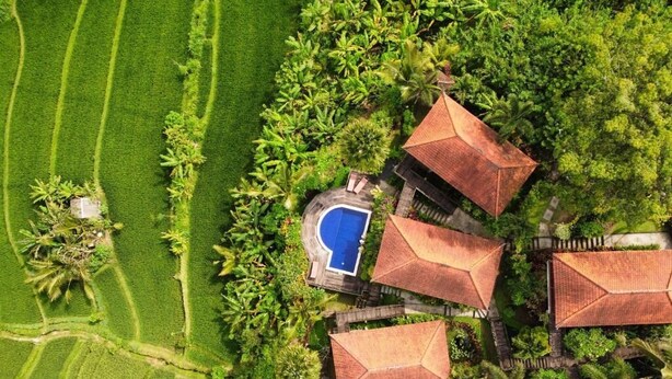 Vista aérea de un resort con varias cabañas, una piscina y campos verdes exuberantes.