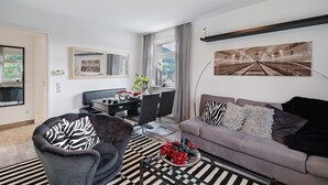 A modern living room with a sofa, armchair, dining table, and a large painting on the wall. - Holiday Apartment 'Baden - Baden International' with Wi-Fi (Baden-Baden)