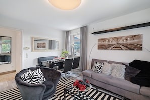 Un salon moderne avec un canapé, un fauteuil, une table à manger et un grand tableau accroché au mur.