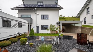 Una casa moderna de dos pisos amb panells solars, un porxo cobert i un jardí paisatjista.