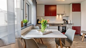 Una cuina moderna amb armaris blancs, una paret d'accent vermella i una zona de dinar amb taula i cadires blanques.