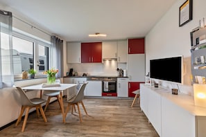 Une cuisine moderne avec des meubles blancs et rouges, une table à manger avec des chaises, un téléviseur et une fenêtre avec des rideaux.