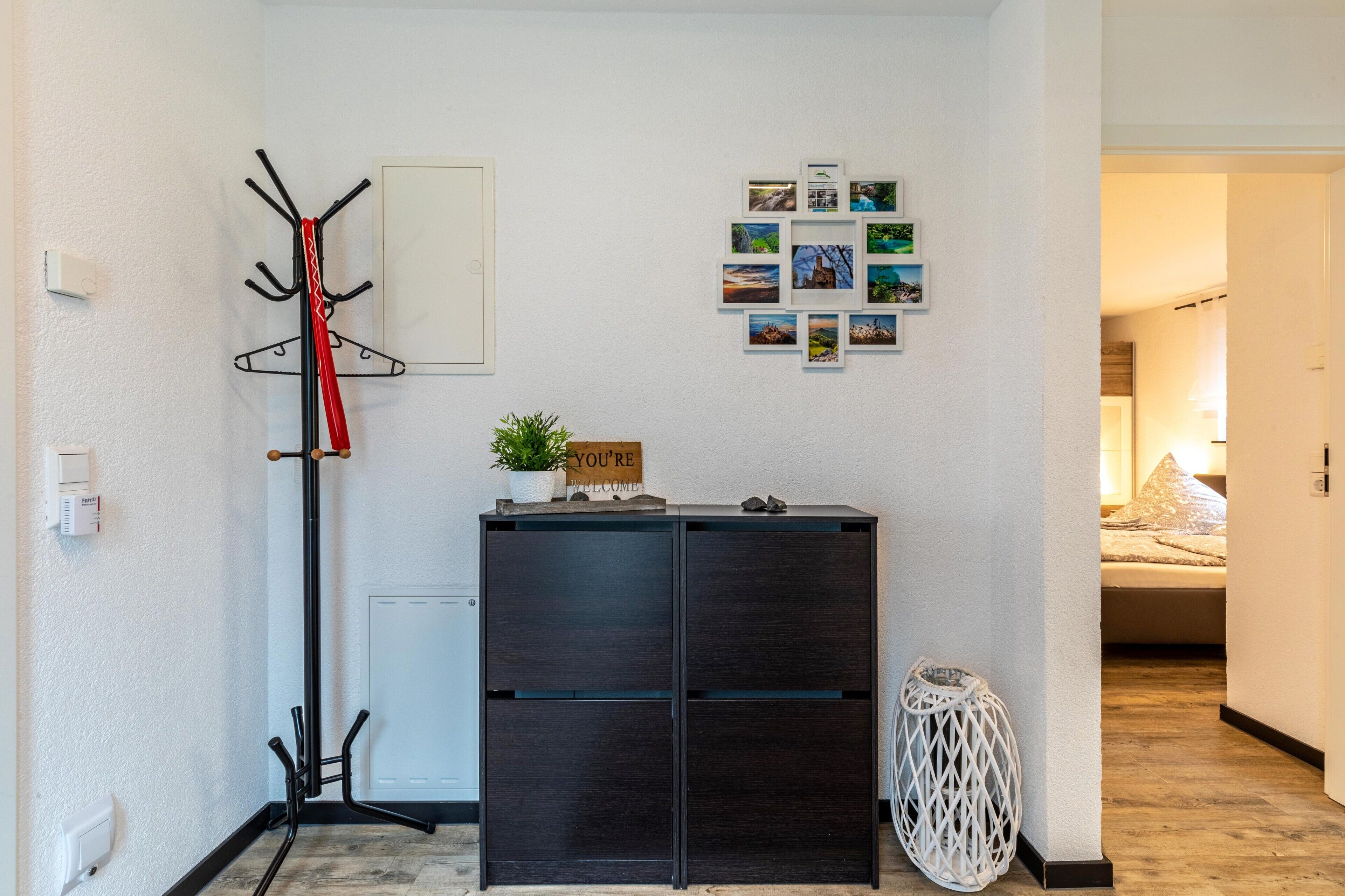 A hallway with a coat rack, a welcome sign, a small plant, and a wall with photos.