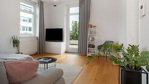 A modern living room with a flat-screen TV, a sofa, a coffee table, a bookshelf, and a potted plant. - Timeless Home: Stylish Oasis Near the Lake (Bregenz)