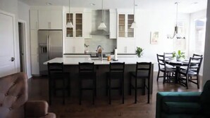 A modern kitchen with white cabinets, a central island with bar stools, and pendant lighting. - Plumberry Cottage in Charming Neighborhood (College Place)