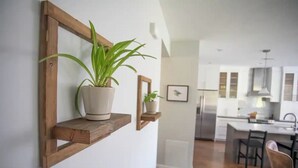 A modern kitchen with wooden shelves, potted plants, and a view into the dining area. - Plumberry Cottage in Charming Neighborhood (College Place)