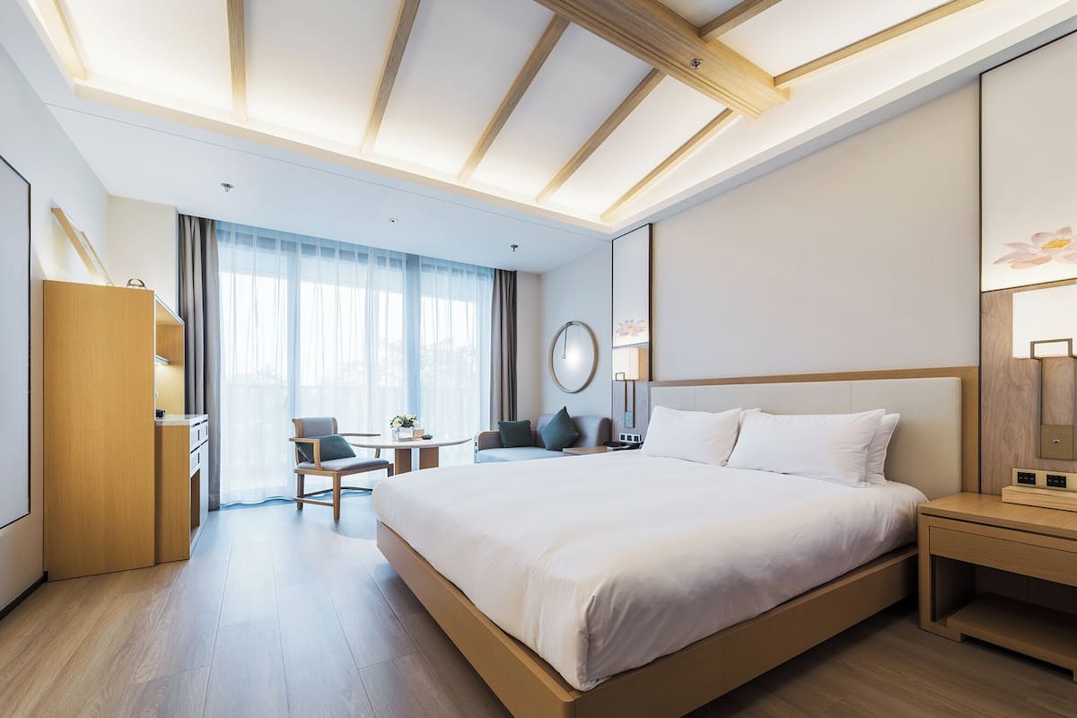 A modern hotel room with a large bed, a desk, a chair, and a wardrobe.