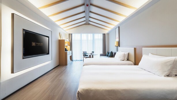 A modern hotel room with a large flat-screen TV, a wooden ceiling, two beds, a seating area with a table, and a view of the outdoors. - HENTIQUE MANNA TANGSHAN (Nanjing)