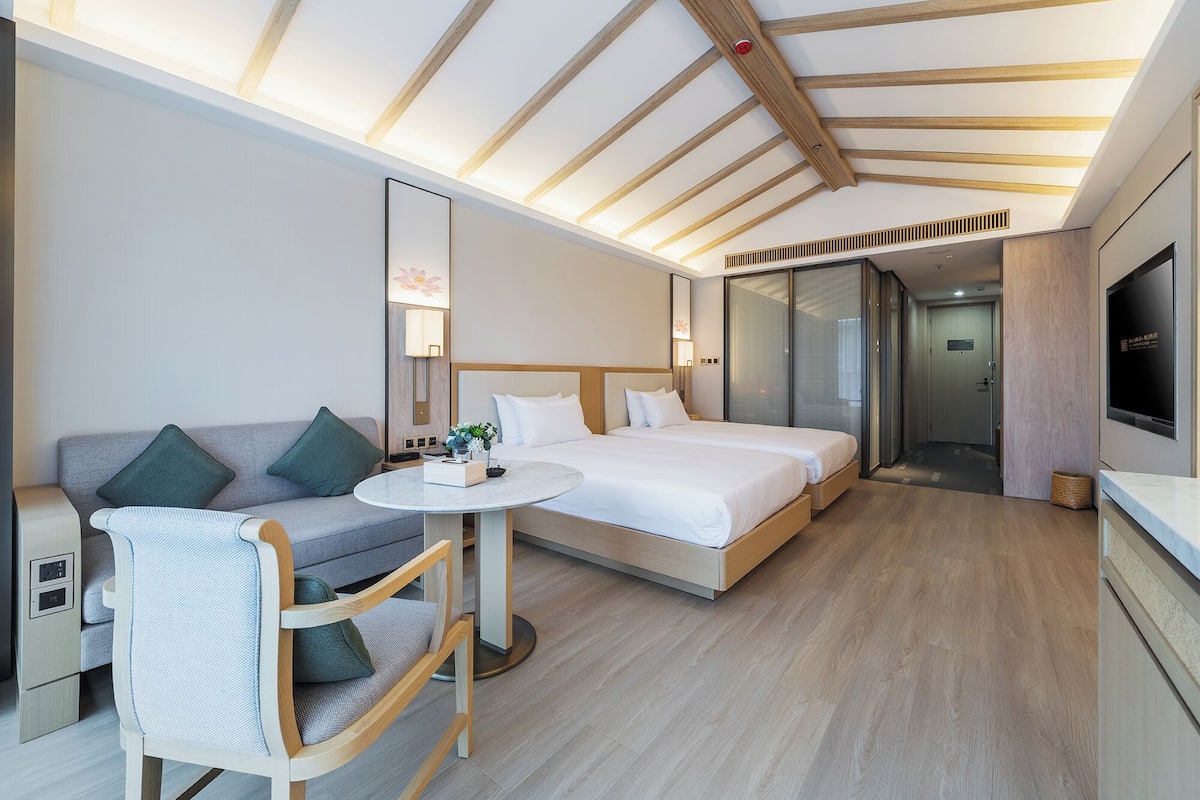 A modern hotel room with a wooden ceiling, a sofa, a round table, two beds, and a TV.