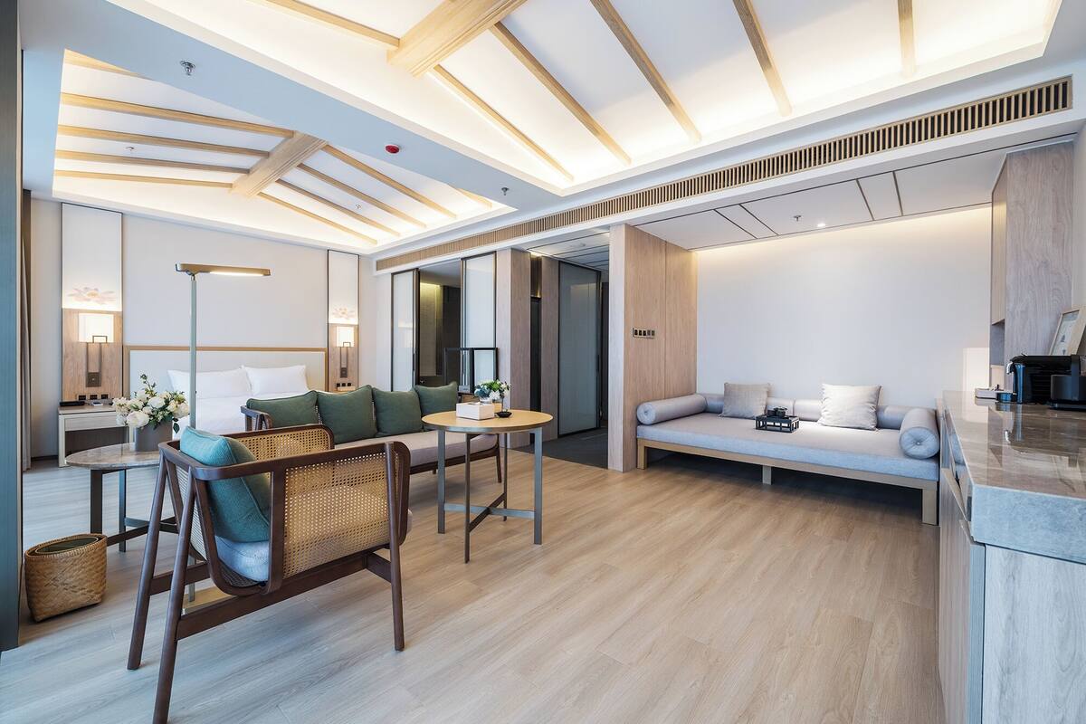 A modern hotel room with a wooden ceiling, a sofa, a dining area, and a large mirror.