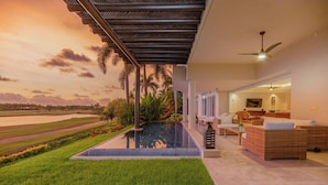 Un espacio exterior moderno con piscina, mobiliario de sala de estar y vistas a un campo de golf al atardecer.