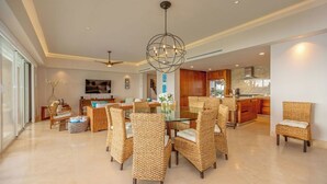 Amplia sala de estar con muebles de mimbre, una mesa de comedor de vidrio y una cocina moderna al fondo.