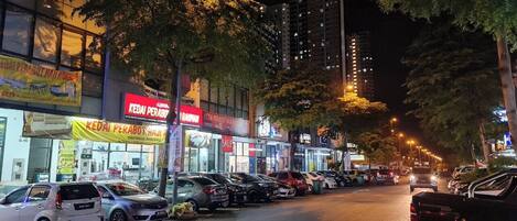 Una calle iluminada de noche, con vehículos estacionados y escaparates brillantes.