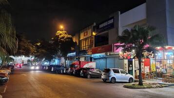 A nighttime street scene with parked cars, a J&T Express store, and a computer store.