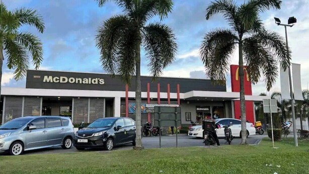 Um restaurante McDonald's com design moderno, com palmeiras em primeiro plano e carros estacionados na frente.