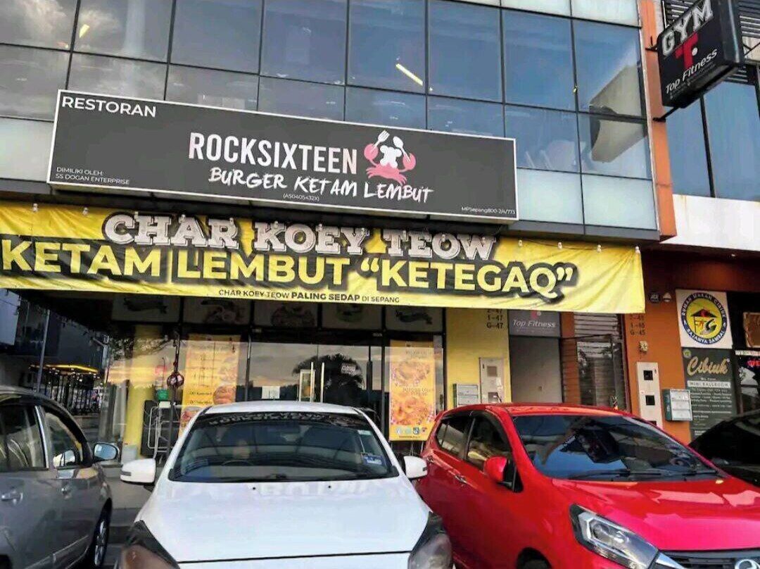 A restaurant named 'ROCKSIXTEEN BURGER KETAM LEMBUT' with a yellow signboard and parked cars in front.