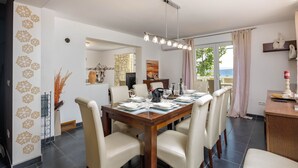 A dining area with a wooden table set for six, surrounded by chairs, with a view of the outdoors through a large window. - Seaview House Helena - Apartment 1, Plomin, Croatia (Plomin)