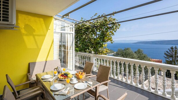 A balcony with a table set for breakfast, a view of the sea, and a yellow wall. - Seaview House Helena - Apartment 1, Plomin, Croatia (Plomin)