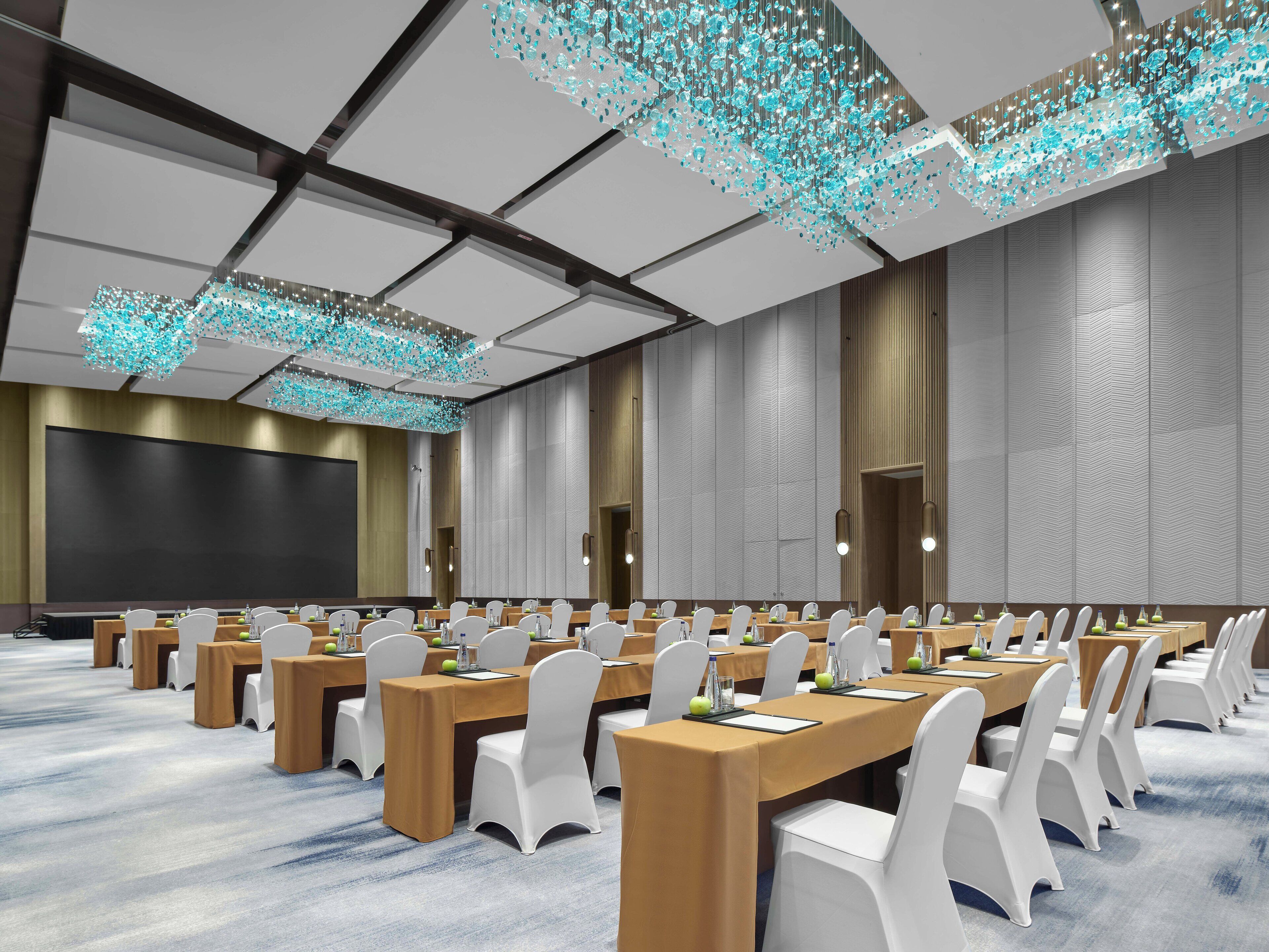Un salón de conferencias con varias mesas, sillas blancas y una pantalla grande.