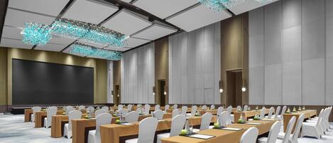 Un salón de conferencias con varias mesas, sillas blancas y una pantalla grande.