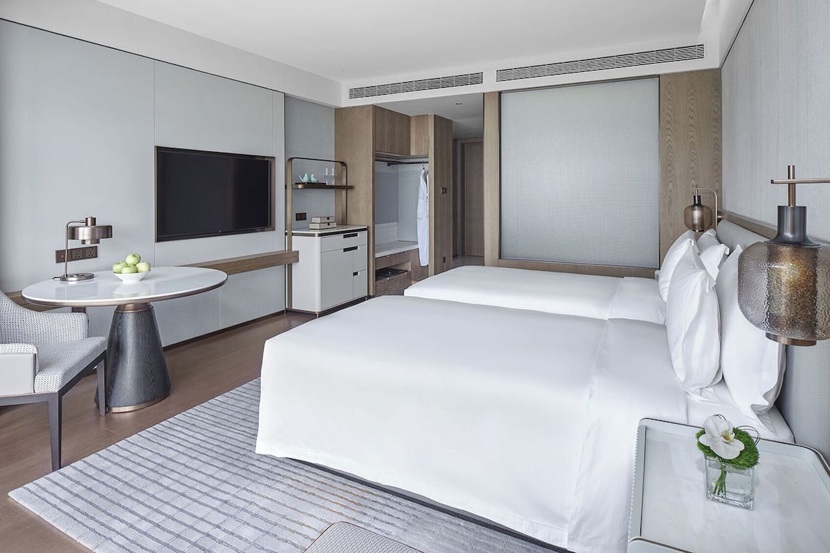 A modern hotel room with a large bed, a desk with a lamp, a TV, and a wardrobe.