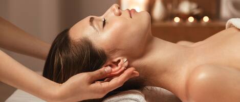 A person lying on a massage table with a towel rolled at the head, in a room with candles in the background.