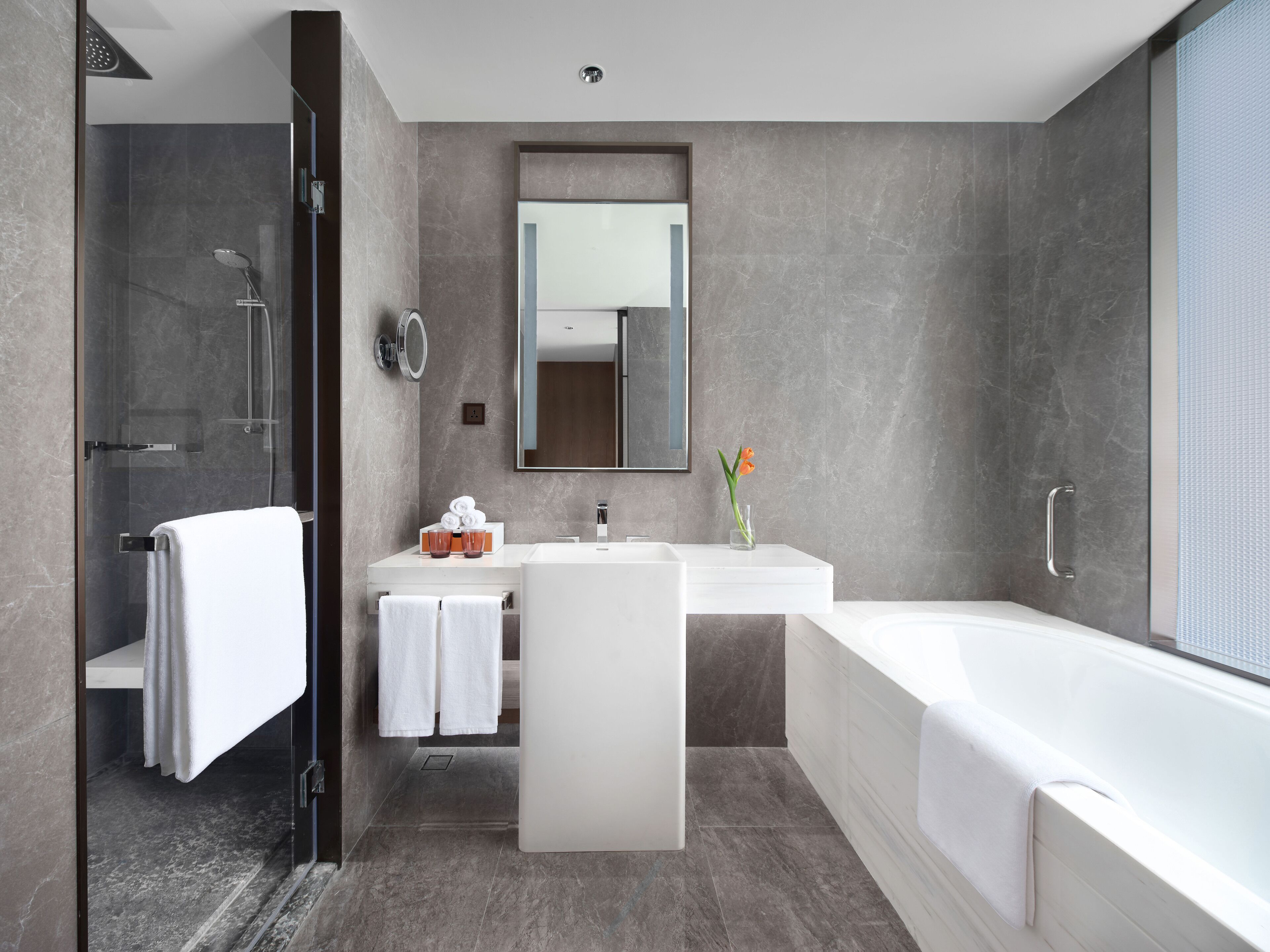 Een moderne badkamer met een douchecabine van glas, een witte wastafel met een grote spiegel en een vrijstaand bad.