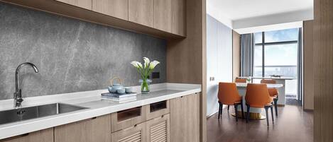 A modern kitchen with wooden cabinets, a white countertop, and a view of a dining area with orange chairs.