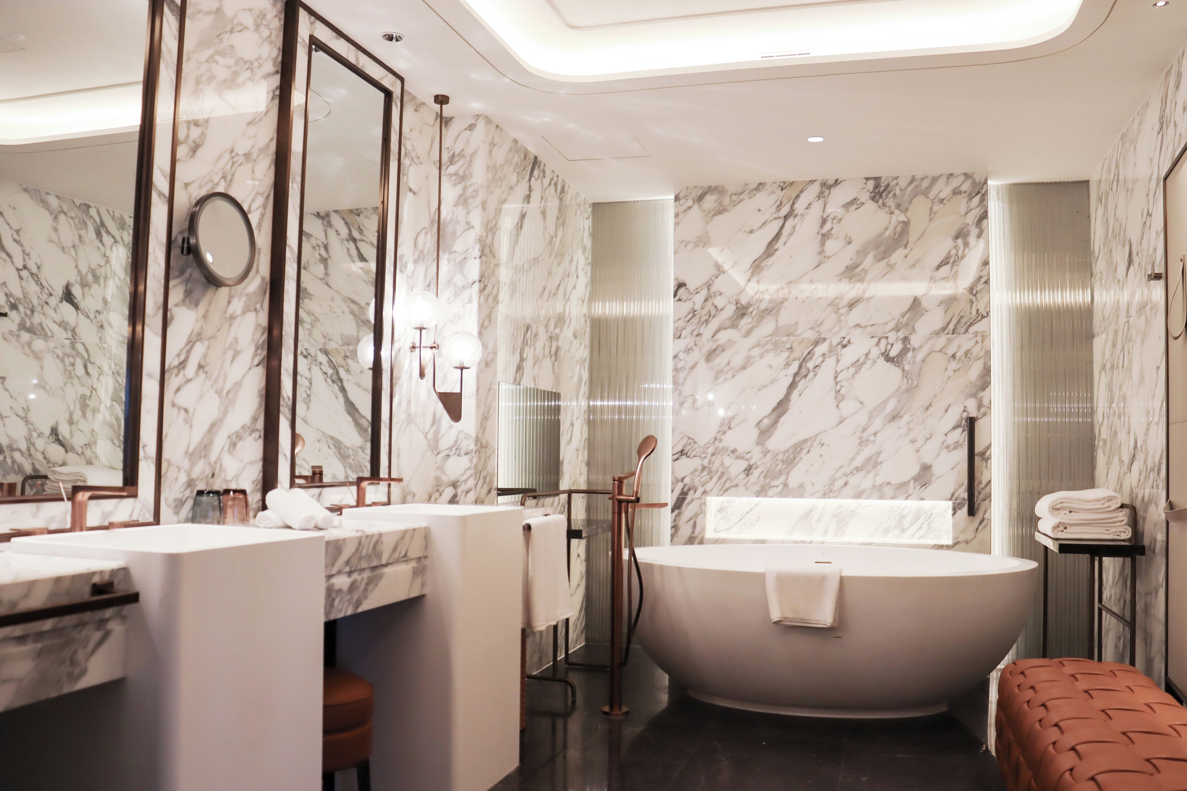 A modern bathroom with marble walls, a freestanding bathtub, and a large mirror.