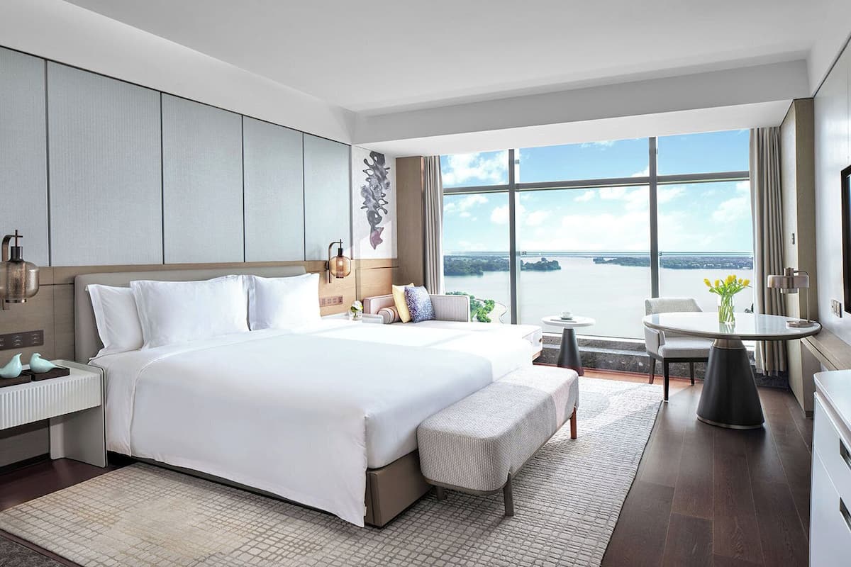 A modern hotel room with a large bed, a small table, and a view of the water.