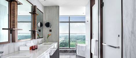 A modern bathroom with a large mirror, two sinks, a shower, and a view of a cityscape.