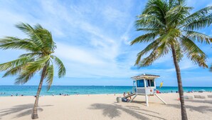A beach with palm trees, a lifeguard tower, and the ocean in the background.