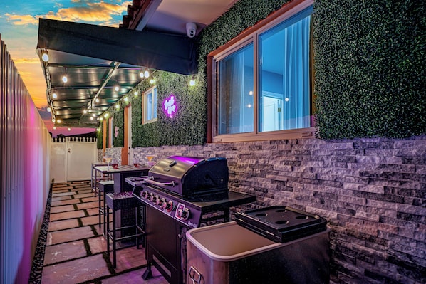 An outdoor patio with a grill, stone pathway, and a window overlooking a garden.