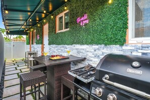 An outdoor patio with a grill, wicker furniture, and a neon sign.