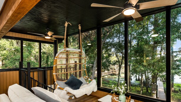 Una habitación amplia con un gran ventanal, un sillón colgante, un sofá y una mesita con un libro y un jarrón.