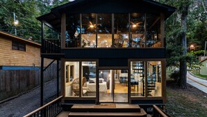 Una casa de madera de dos pisos con ventanas grandes, un balcón y una escalera que conduce al nivel superior.