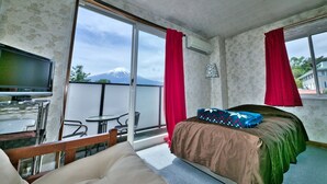 A hotel room with a bed, a sofa, a TV, and a balcony with a view of a mountain. - Hotel CAMELOT (Fujikawaguchiko)