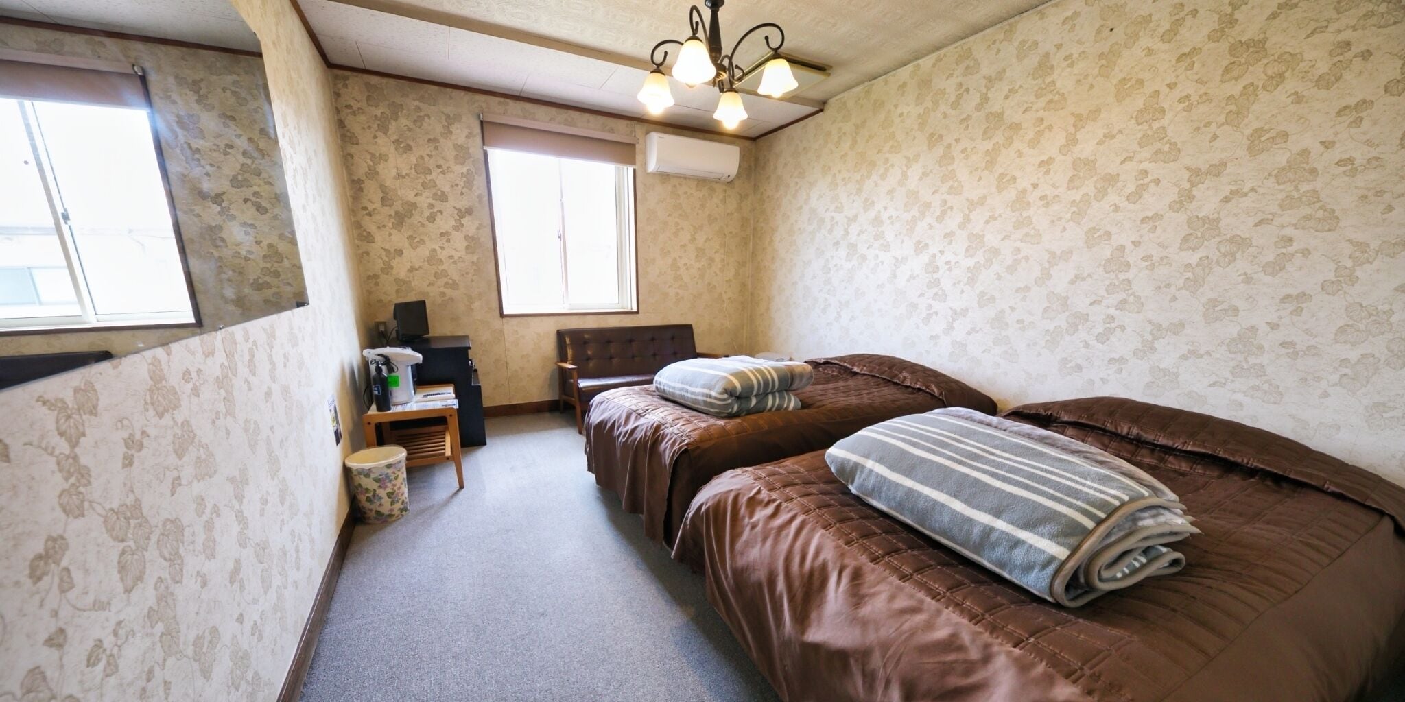 A bedroom with two beds, a desk with a computer, a chair, and a window.