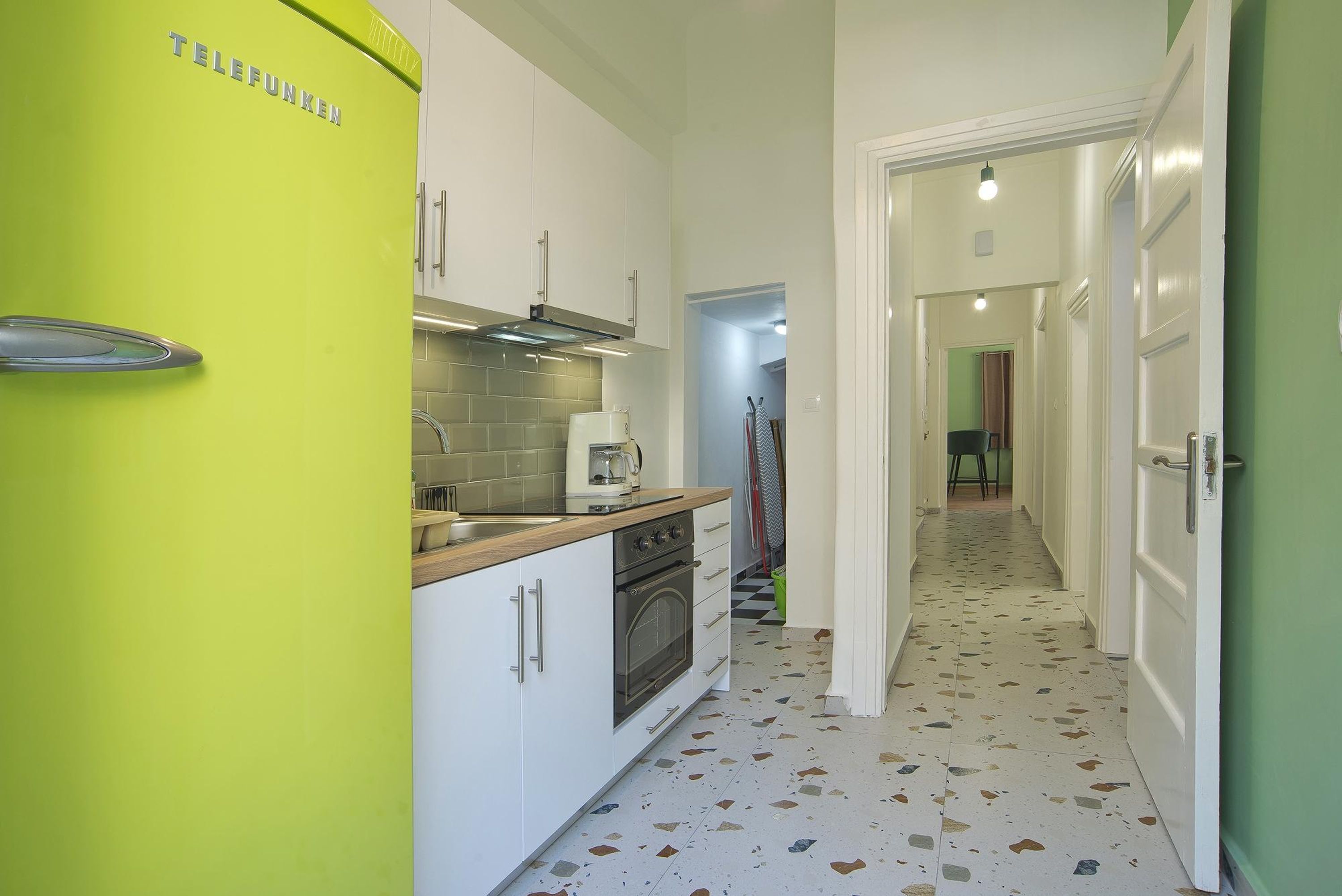 Una cocina pequeña con un refrigerador verde, gabinetes blancos y un salpicadero de azulejos.